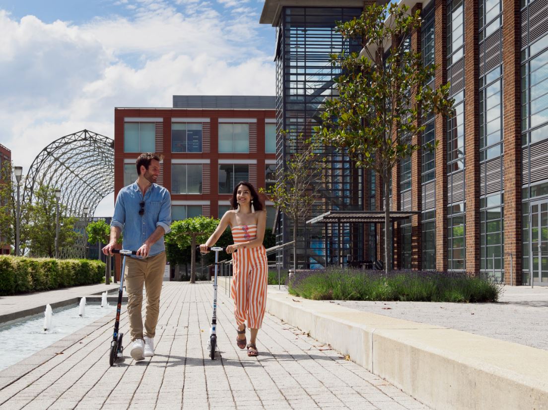 A man and a lady riding a scooter at a business park