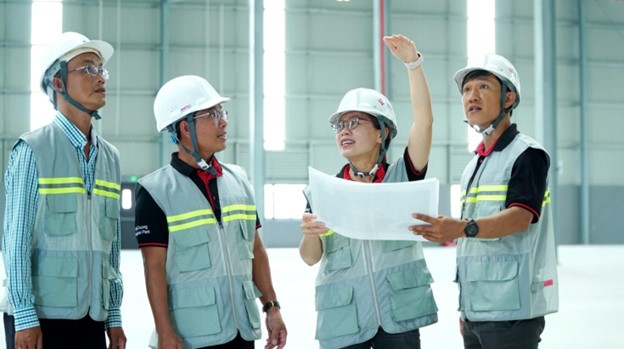 A group of employees in hard hats having a discussion in an industrial warehouse